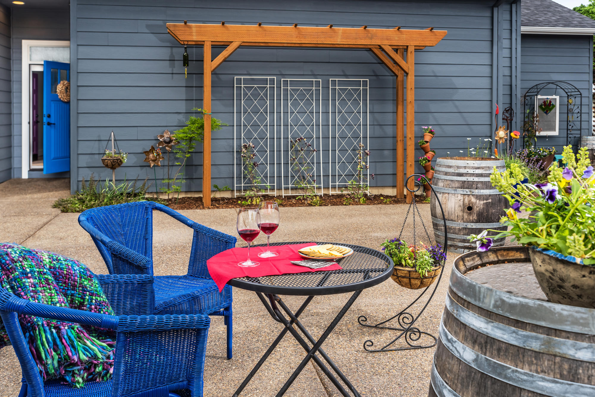 Patio with blue wicker chairs at a small table, plants, wine barrels.
