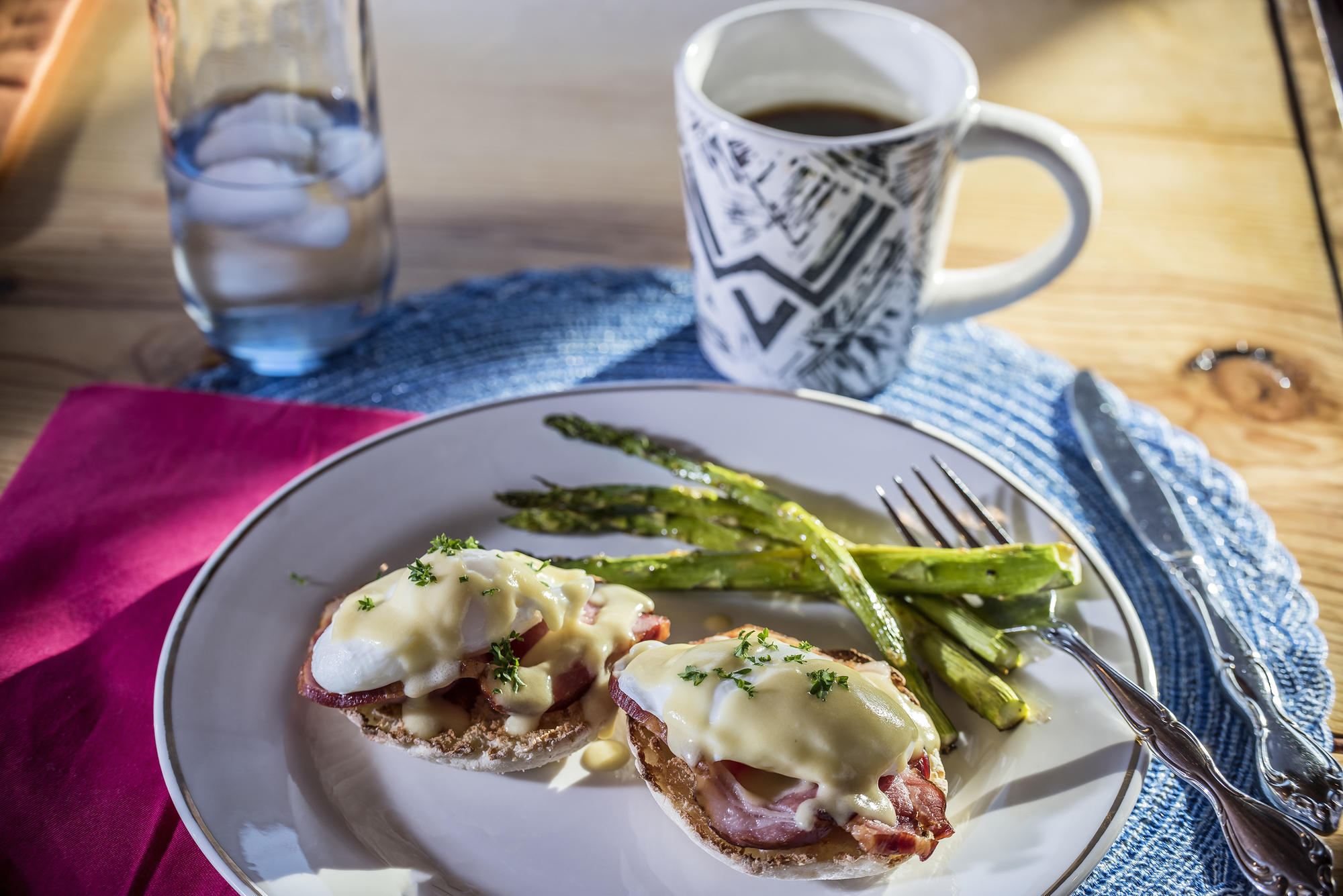 Two English muffin halves with ham and hollandaise sauce with asparagus