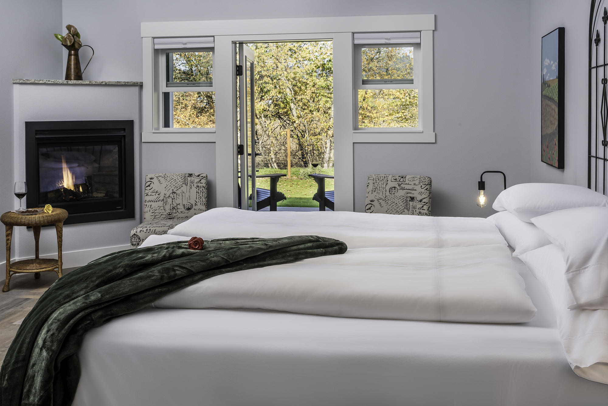 A king bed with white sheets and a green blanket next to a fireplace.