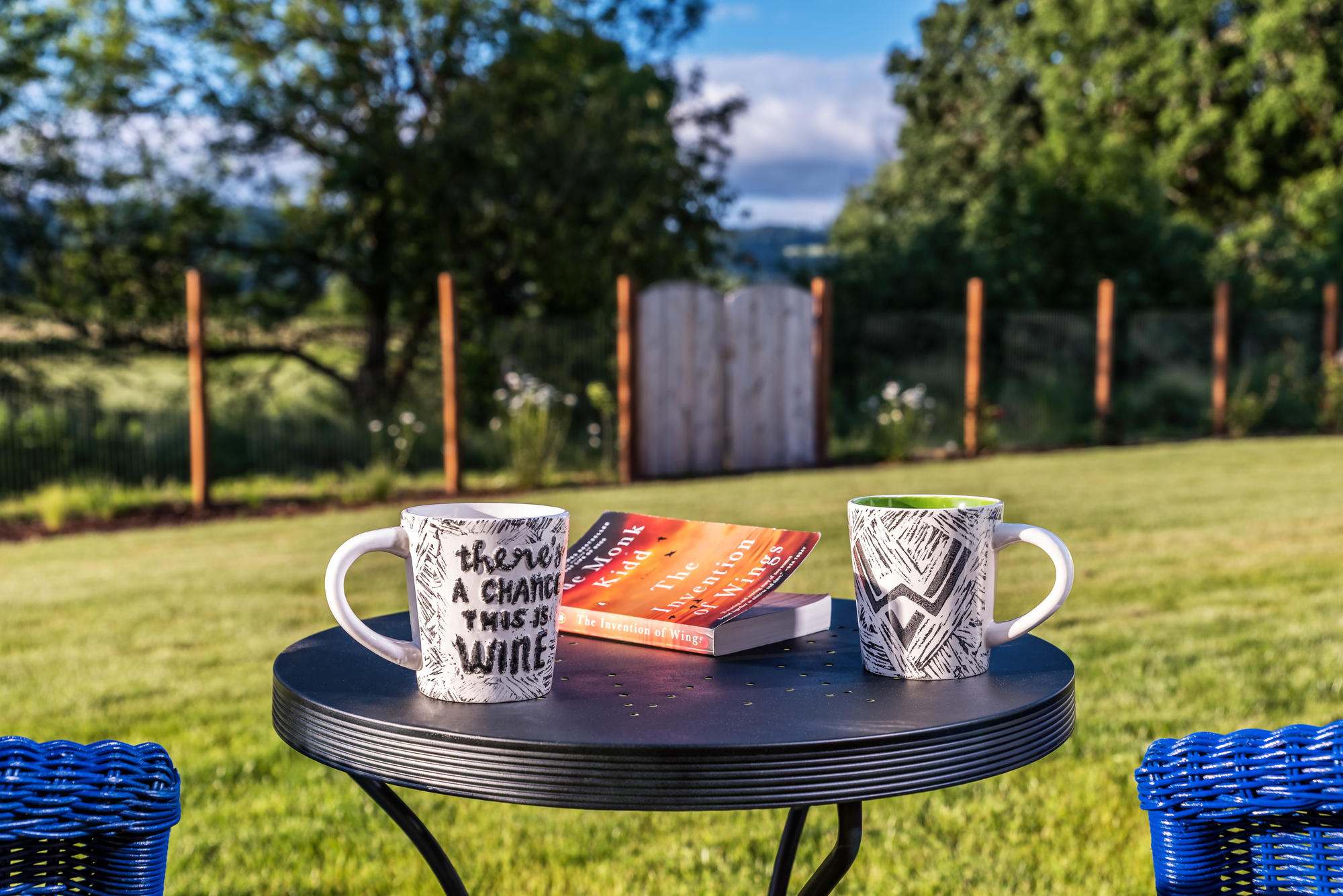 Two coffee mugs on a table with backyard and fence in the background.