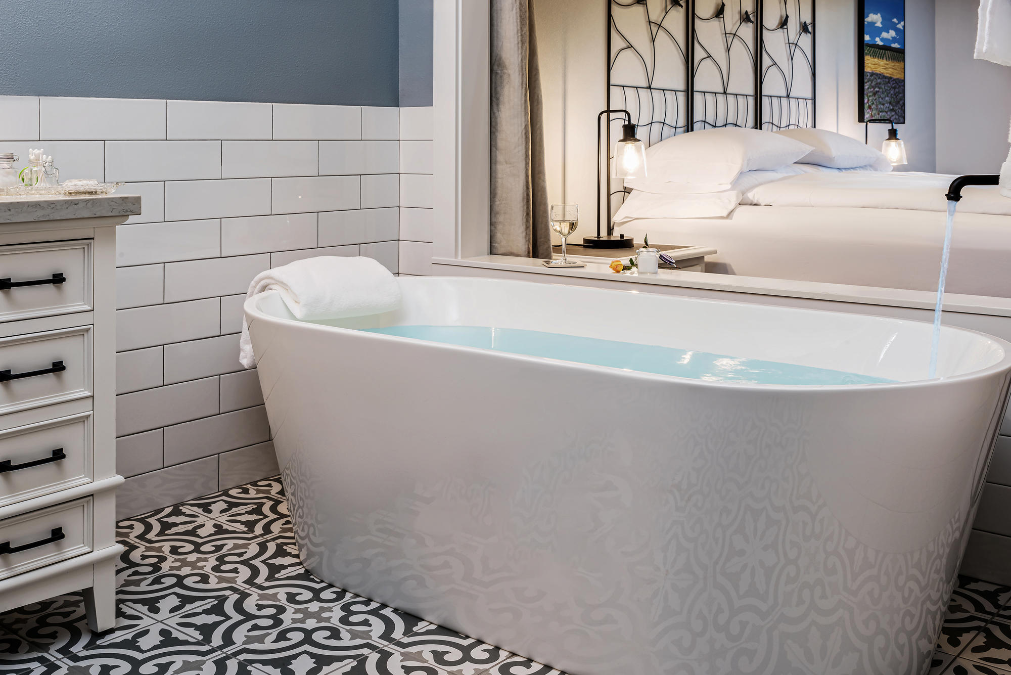 A white soaking bathtub with running water and a glass of white wine.